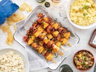 Overhead view of BBQ Chicken Kebabs on a tray surrounded by side dishes.