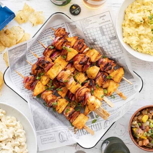 Overhead view of BBQ Chicken Kebabs on a tray surrounded by side dishes.