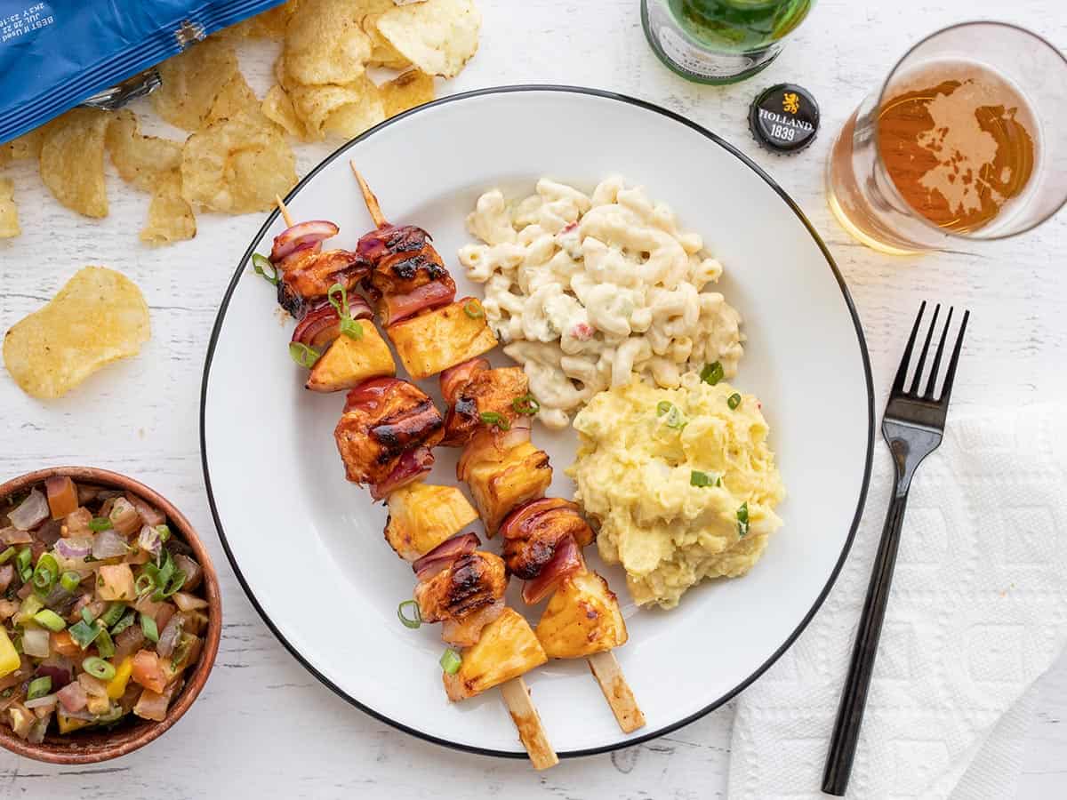 BBQ Chicken Kebabs on a plate with sides, chips, and beer.