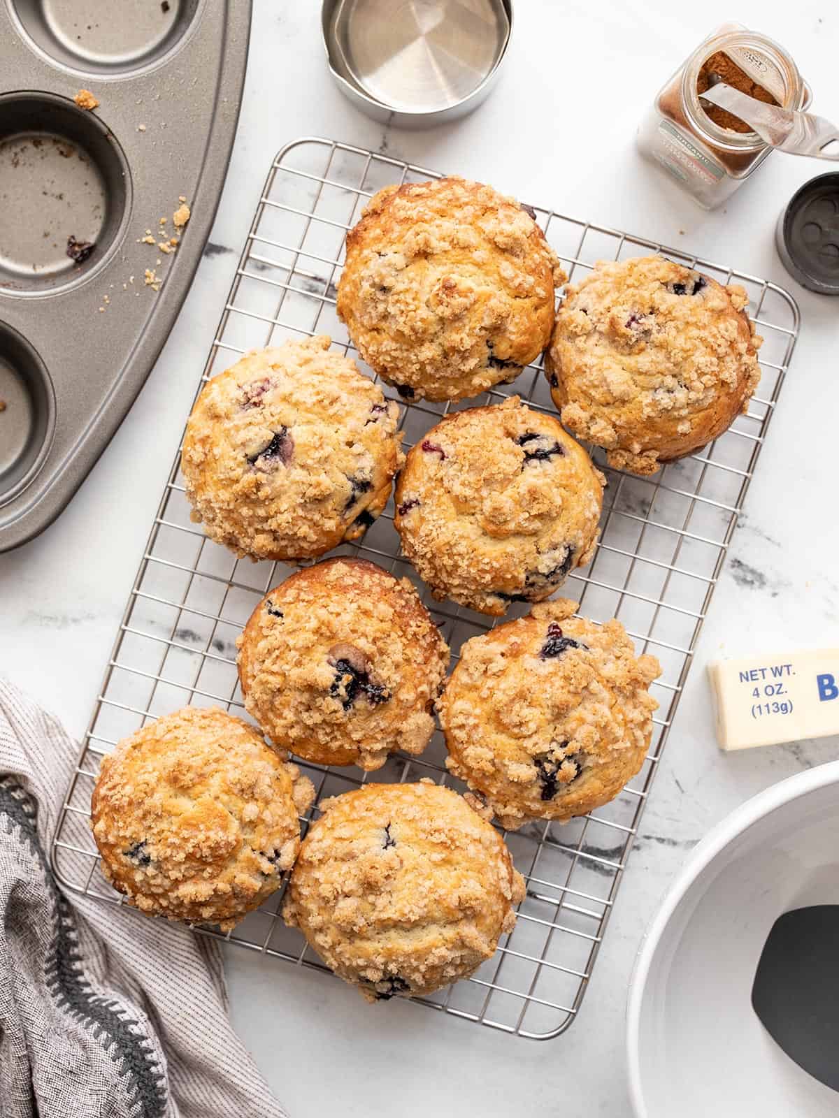 Muffins de mirtilo assados ​​em uma gradinha cercada por suprimentos de panificação.