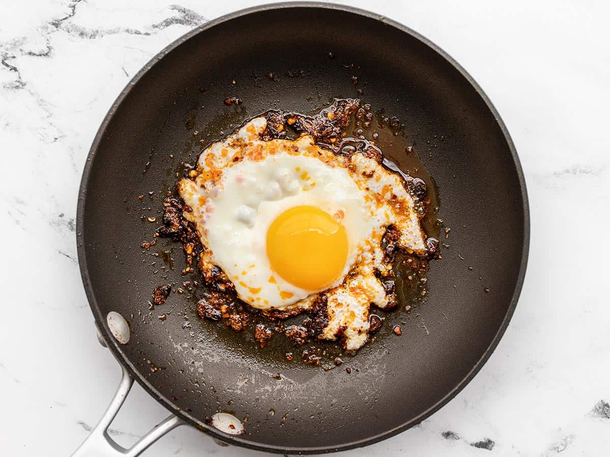 A sunny side up egg being fried in chili crisp.
