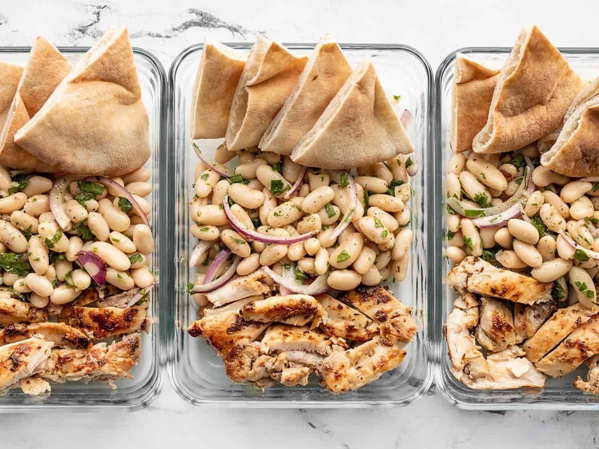 White bean salad in meal prep containers with chicken and pita.