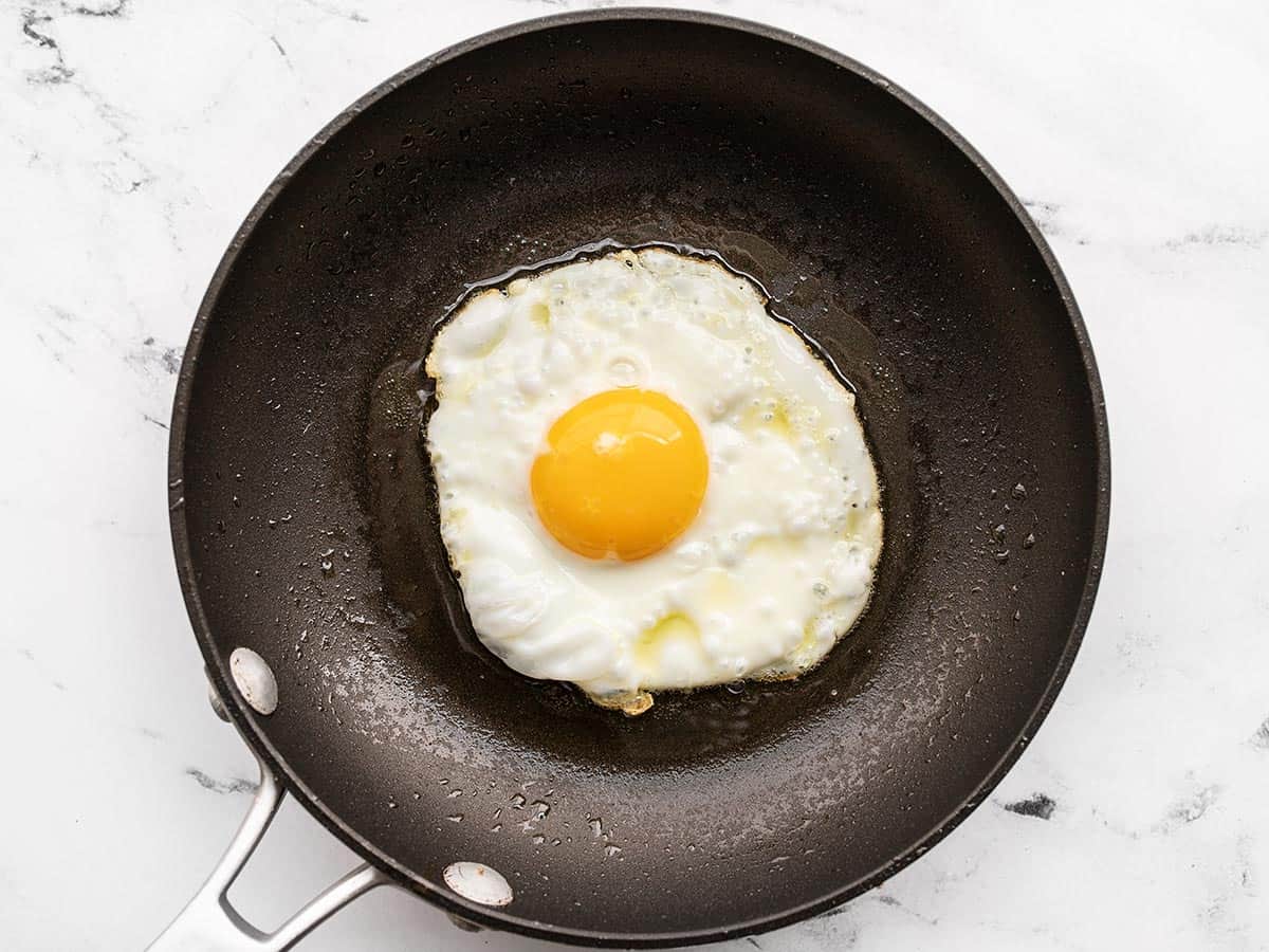 A sunny side up egg being fried in olive oil