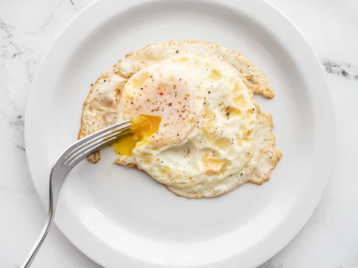 An over easy egg on a plate with a fork piercing the yolk.