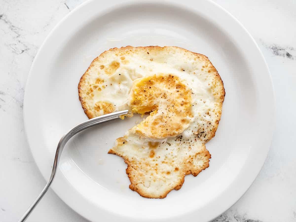 Um ovo cozido duro em um prato com um garfo perfurando a gema cozida.