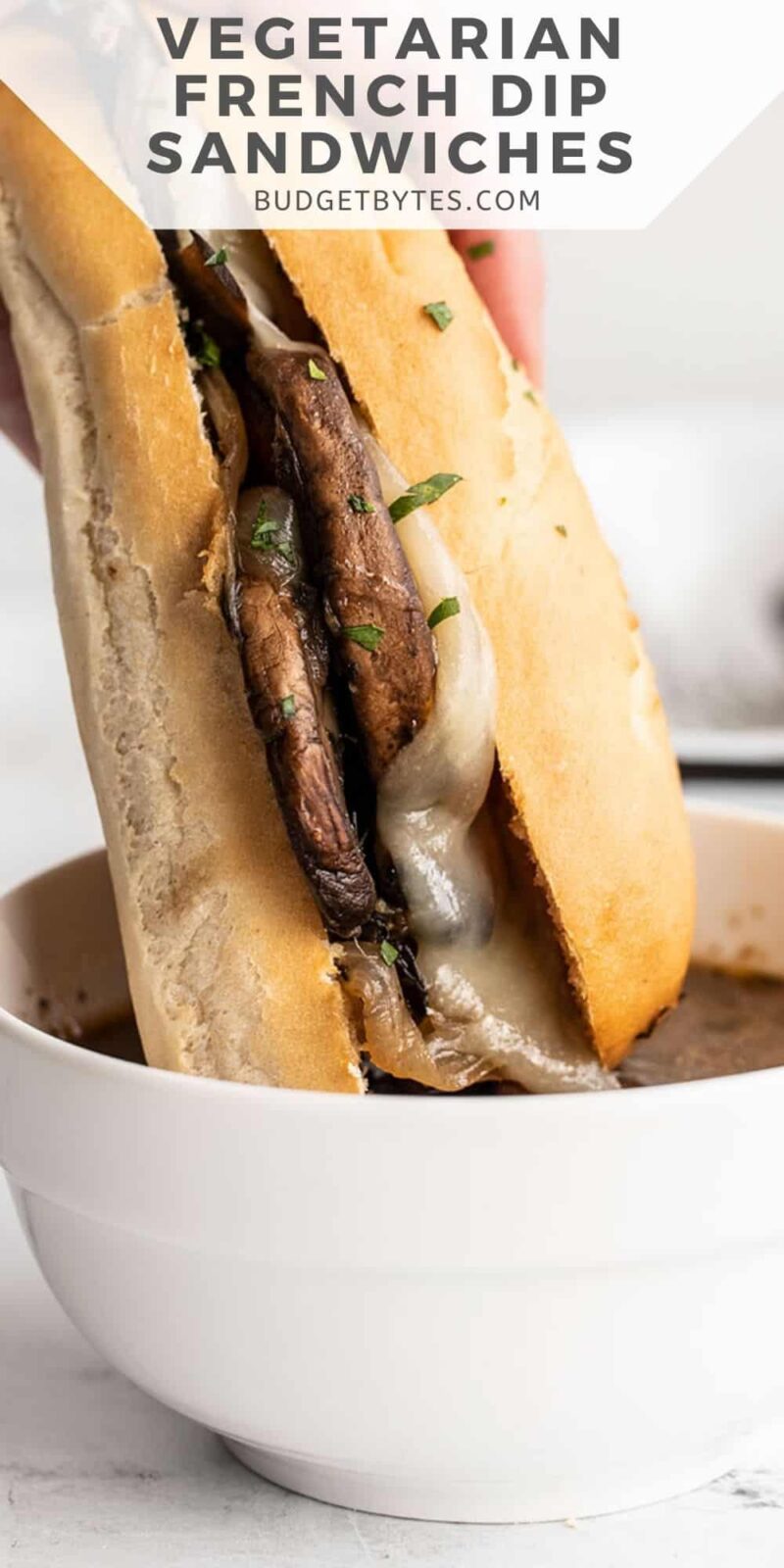 close up of a vegetarian french dip sandwich being dipped into broth.