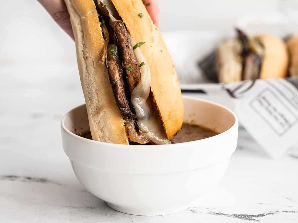 A vegetarian French dip sandwich being dipped into a bowl of au jus.