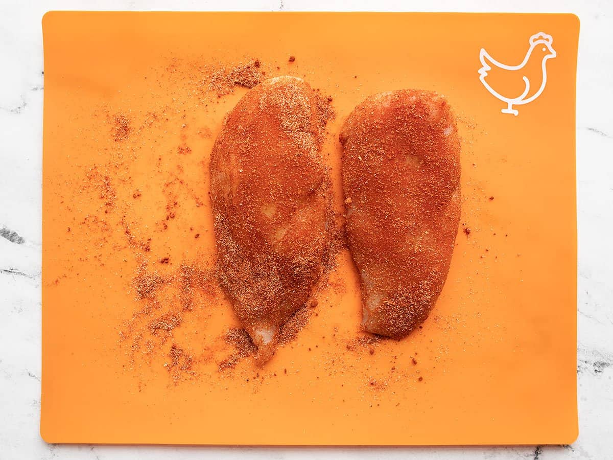 Seasoned chicken breasts on an orange cutting board.