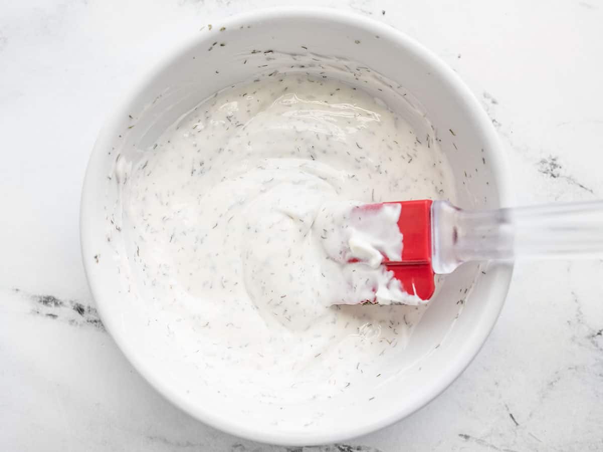 Sour cream and dill dressing in a bowl with a red spatula.