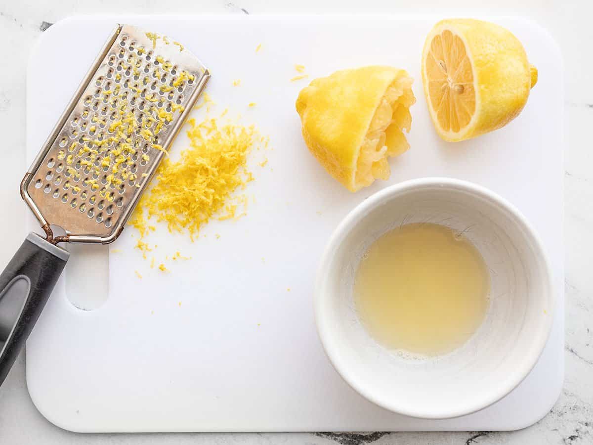 A zested and juiced lemon on a cutting board.