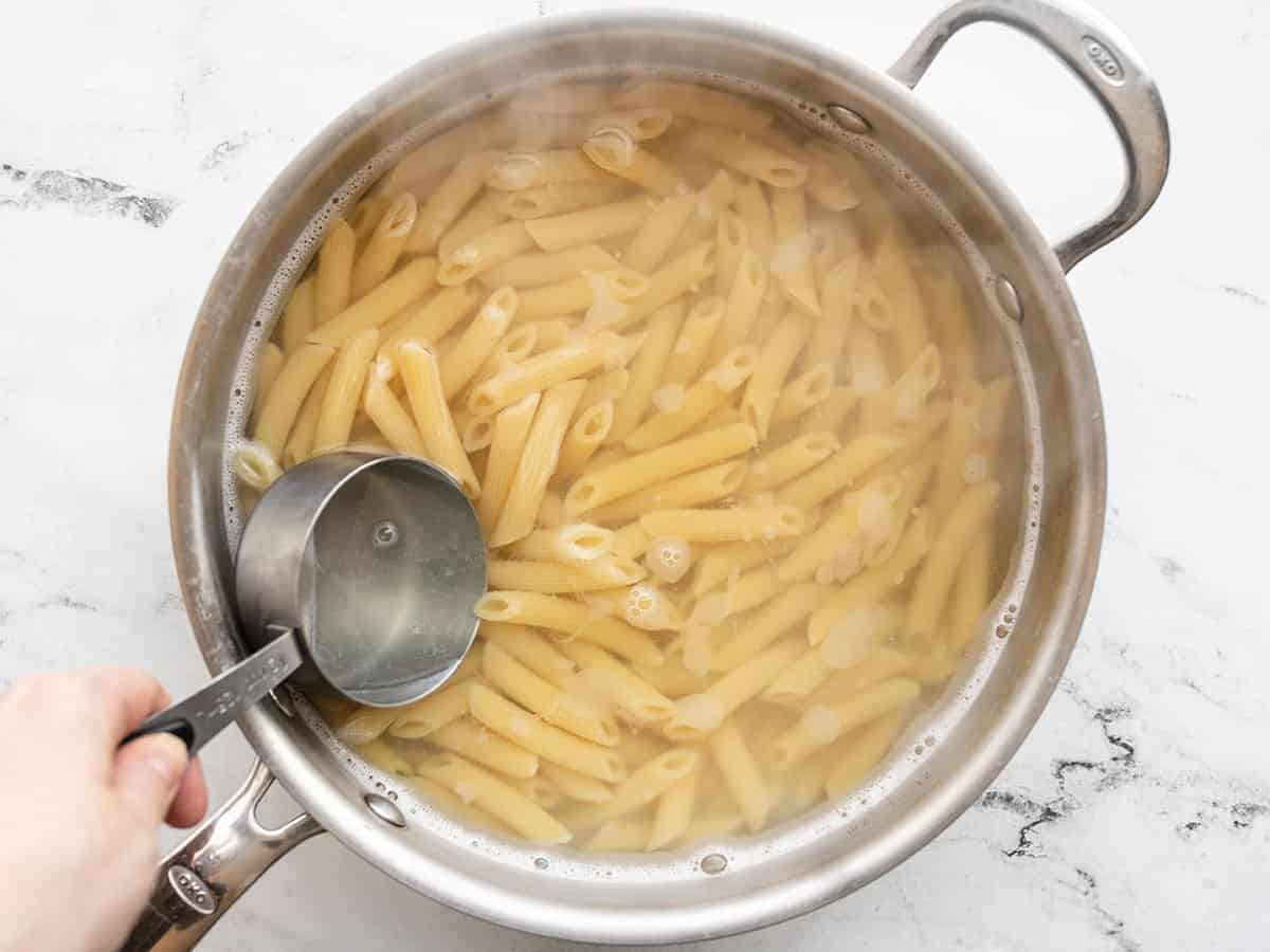 Macarrão cozido em uma panela, a água sendo retirada com um copo medidor.