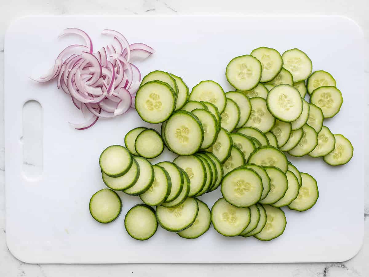 Sliced cucumber and red onion on a cutting board.
