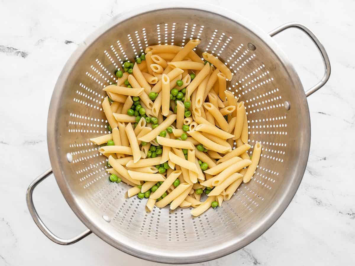Peas and cooked pasta in a colander.