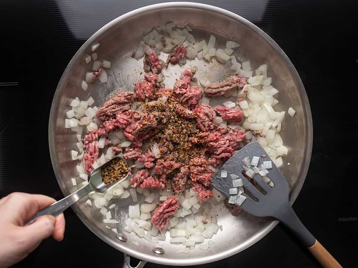 Ground beef in the skillet, steak seasoning being sprinkled over top.