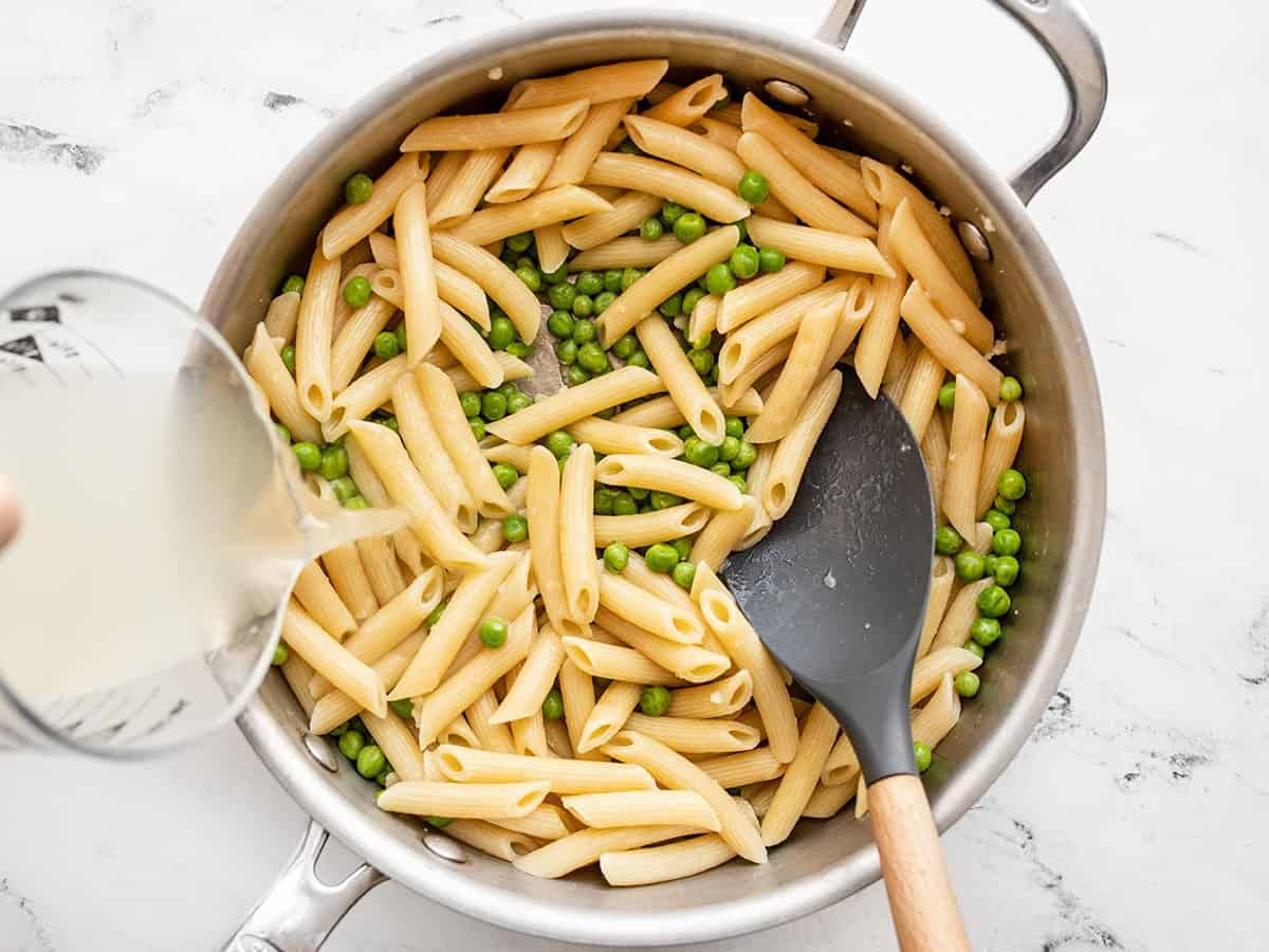 Macarrão, ervilhas e água do macarrão adicionados à frigideira.