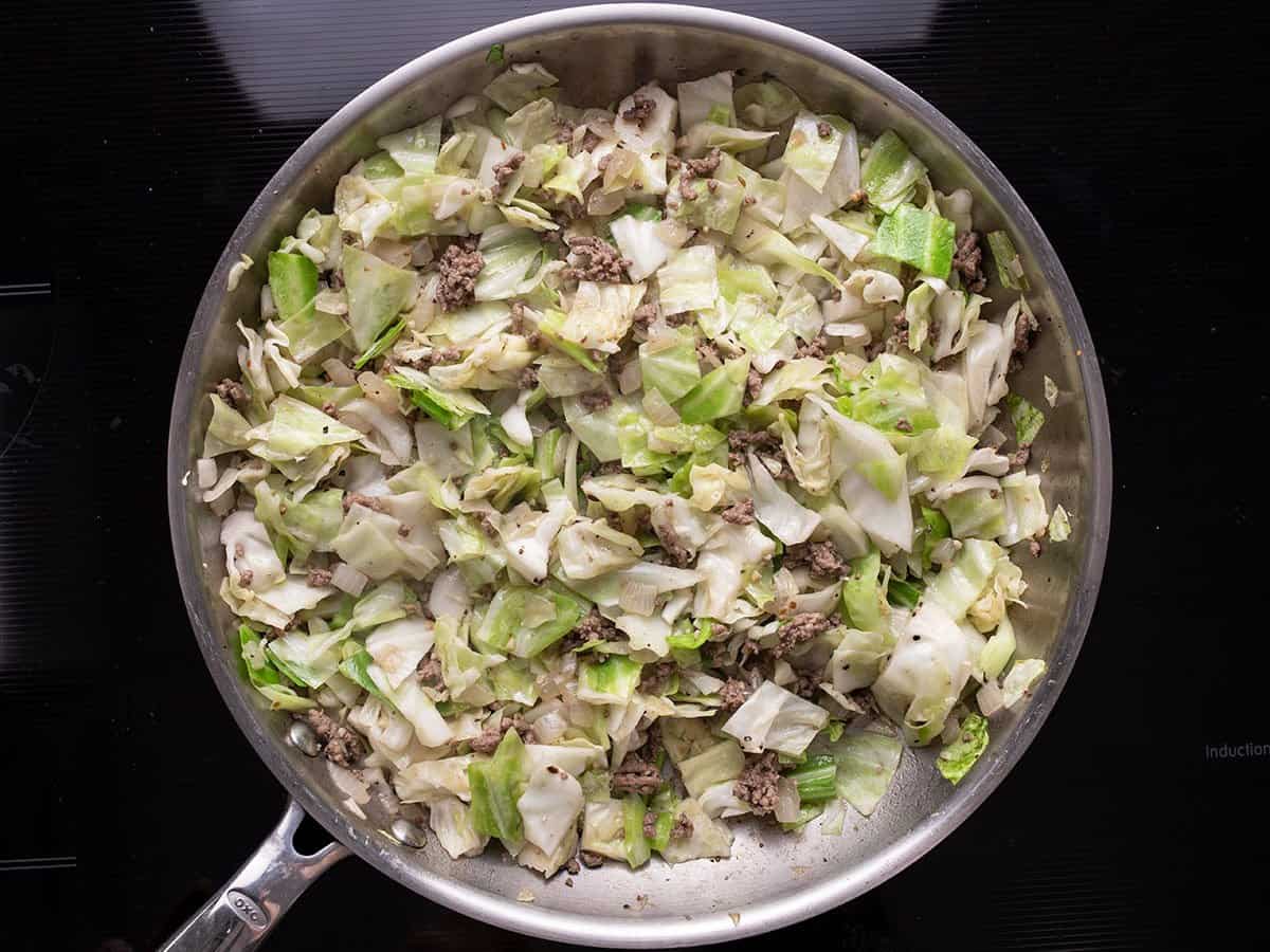 Repolho amolecido misturado com carne e cebola na frigideira.