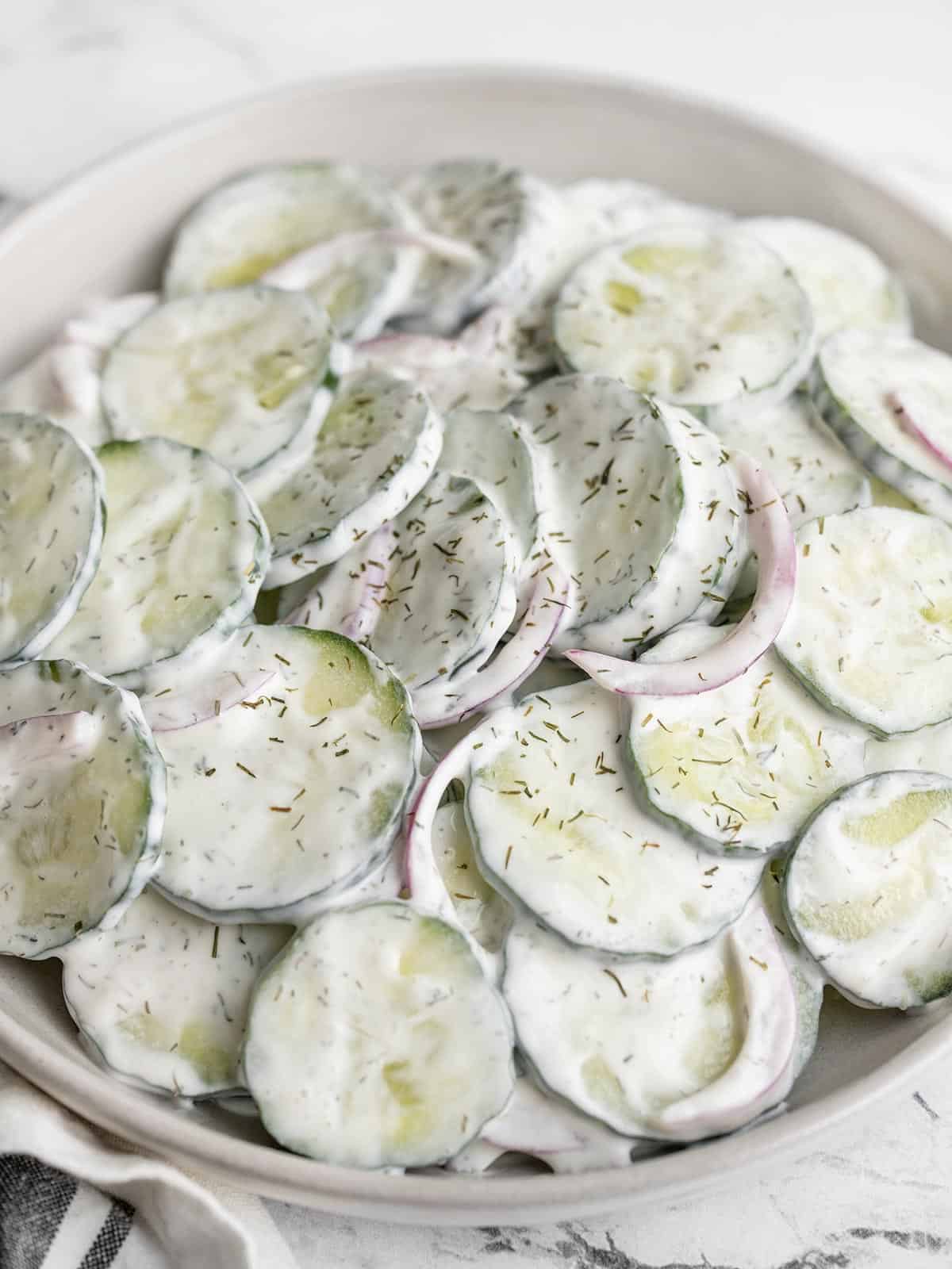 Close up front view of a shallow bowl full of creamy cucumber salad.