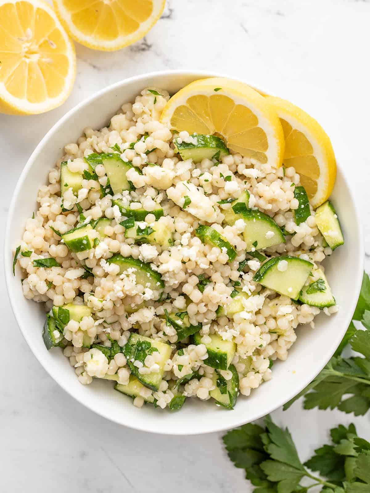 Overhead view of a bowl of lemony cucumber couscous salad with lemons on the side.