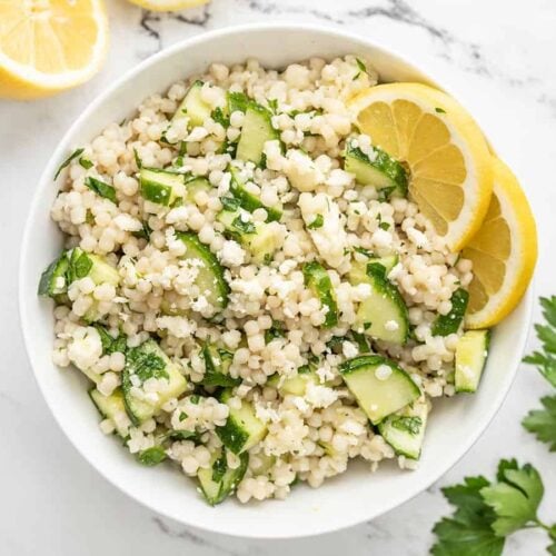 Overhead view of lemony cucumber couscous salad in a bowl garnished with lemons.