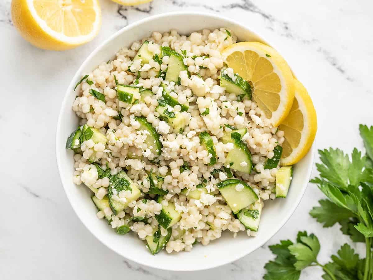 Overhead view of lemony cucumber couscous salad in a bowl garnished with lemons.