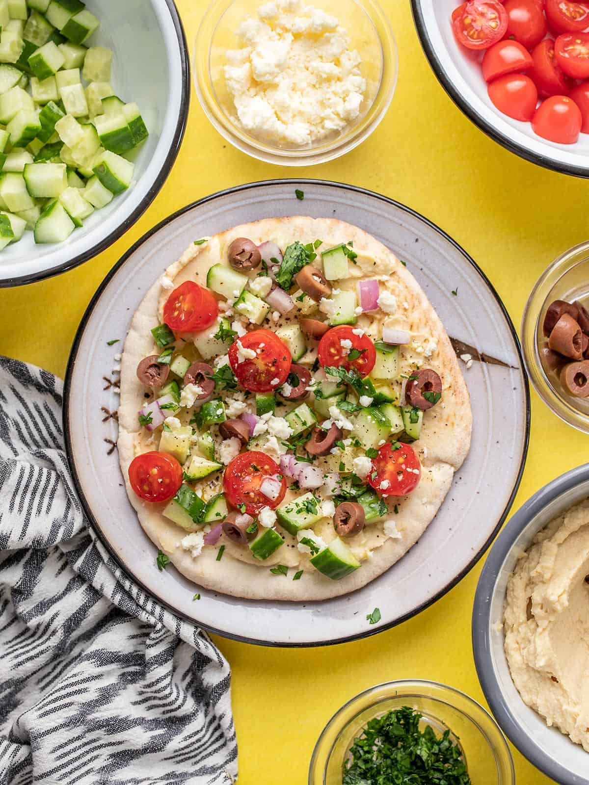 Loaded hummus pita on a plate surrounded by ingredients.