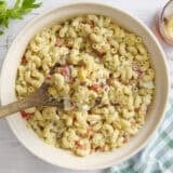 Overhead view of a bowl of macaroni salad with a wooden spoon taking some.