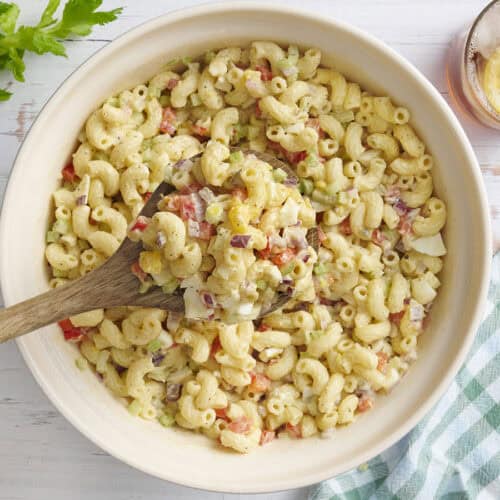 Overhead view of a bowl of macaroni salad with a wooden spoon taking some.