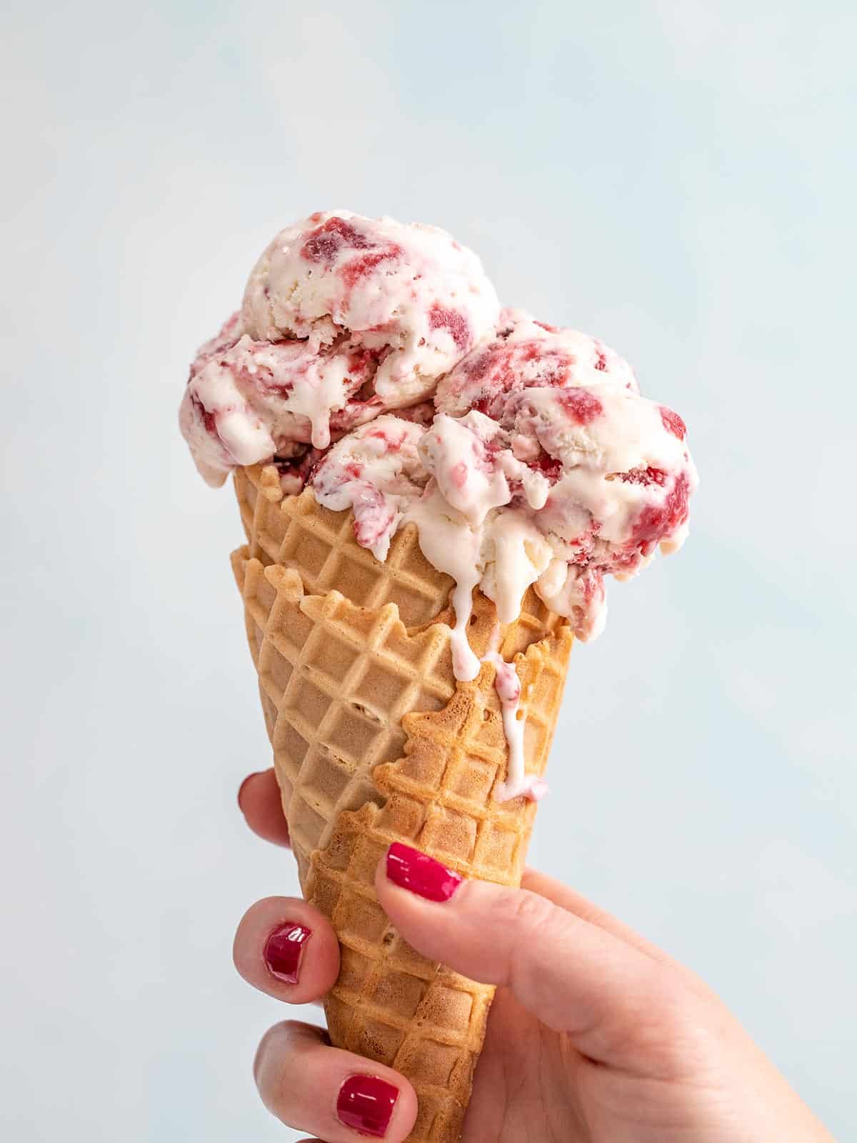 Side view of a hand holding a no-churn strawberry ice cream cone.