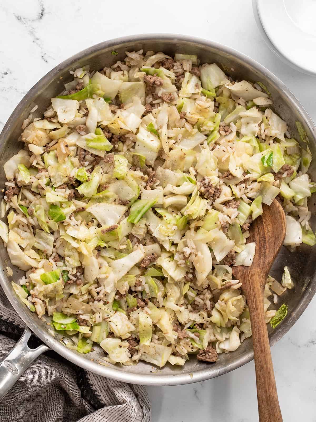 Overhead view of a skillet full of sautéed beef cabbage and rice with a wooden spoon.