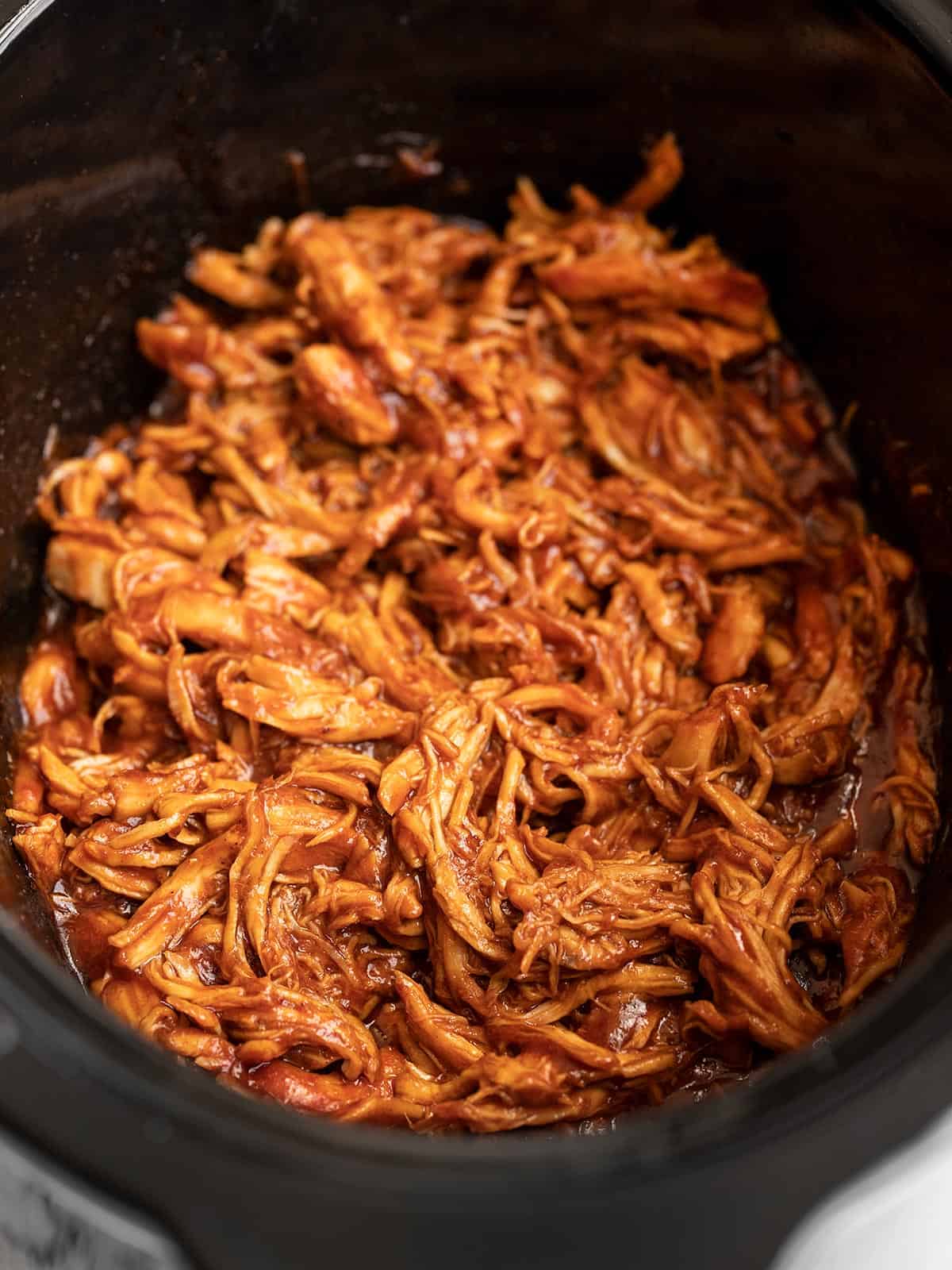 Side view of shredded bbq chicken in a slow cooker.