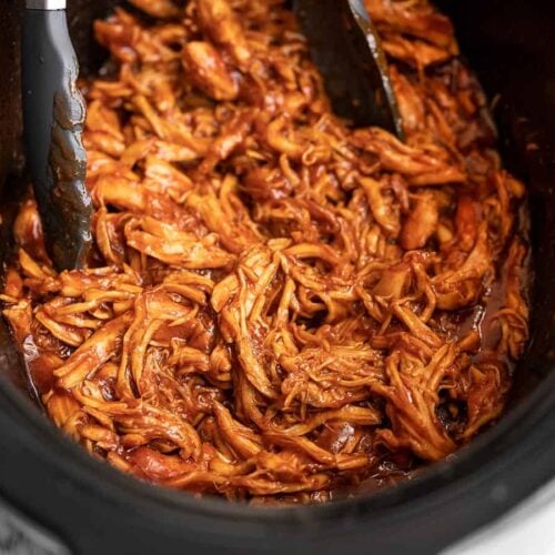 Side view of Slow Cooker BBQ Chicken in the slow cooker with tongs.