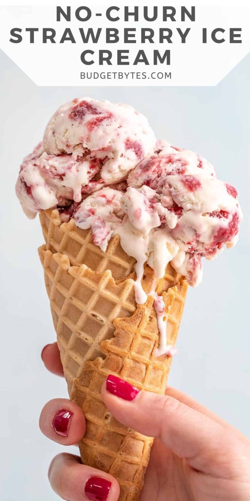 Side view of a hand holding a strawberry ice cream cone.