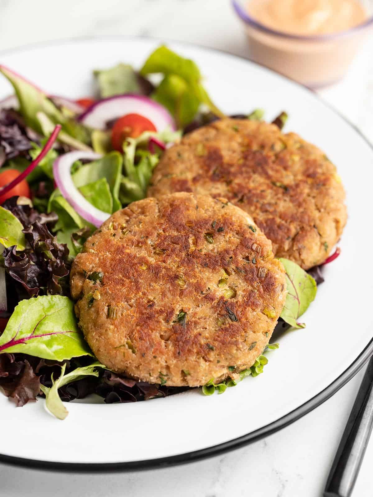 Side view of two tuna cakes on a plate of greens.