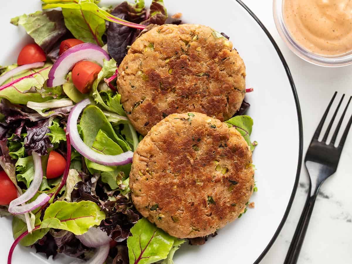 Overhead view of two tuna patties on a plate with greens.