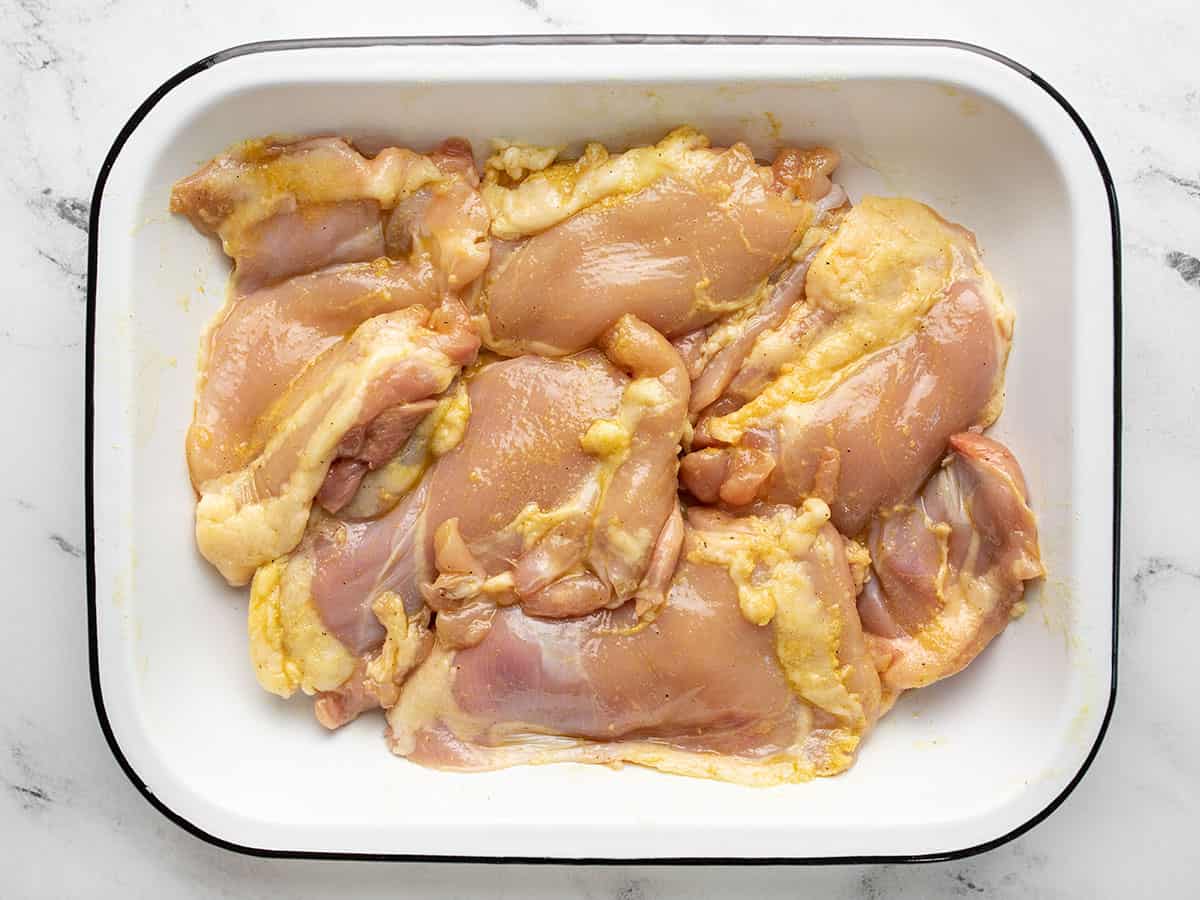 Raw chicken marinating in a white dish.