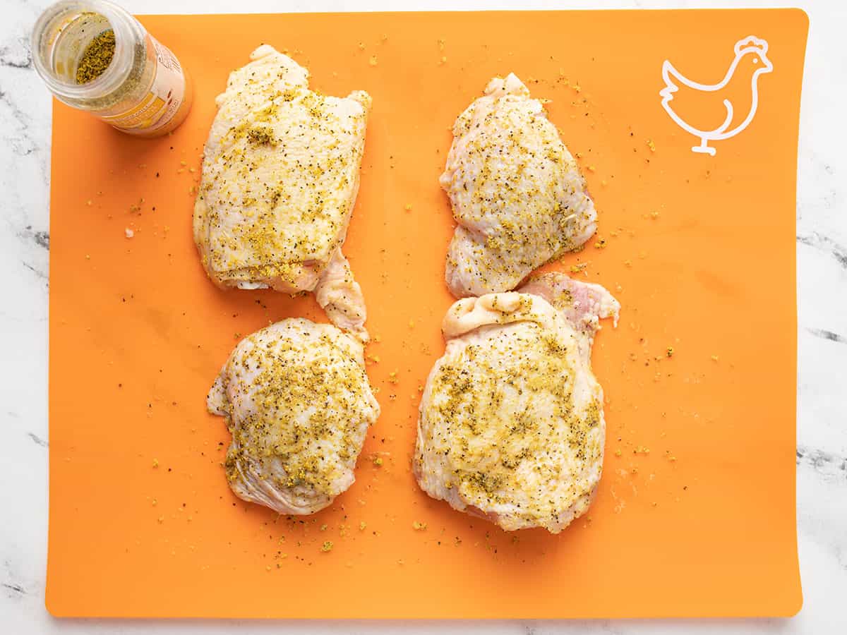 Bone-in chicken thighs seasoned with lemon pepper on a cutting board.