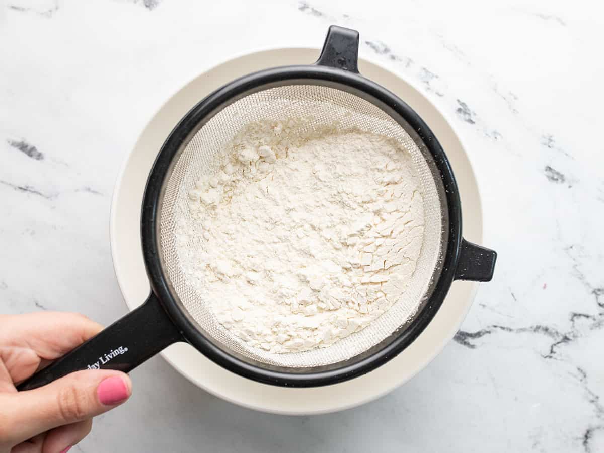 Flour being sifted into a white bowl.