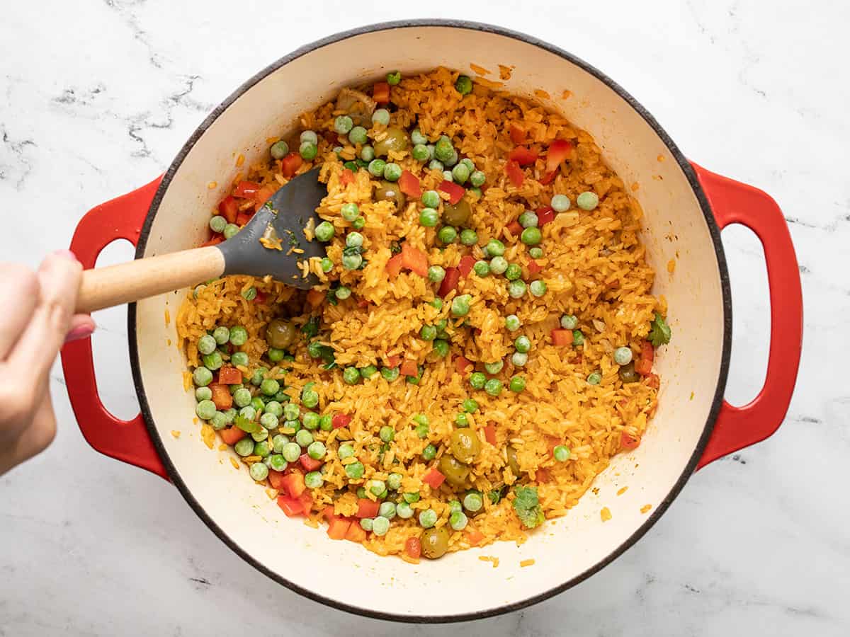 Green peas being stirred into rice in a red Dutch oven.