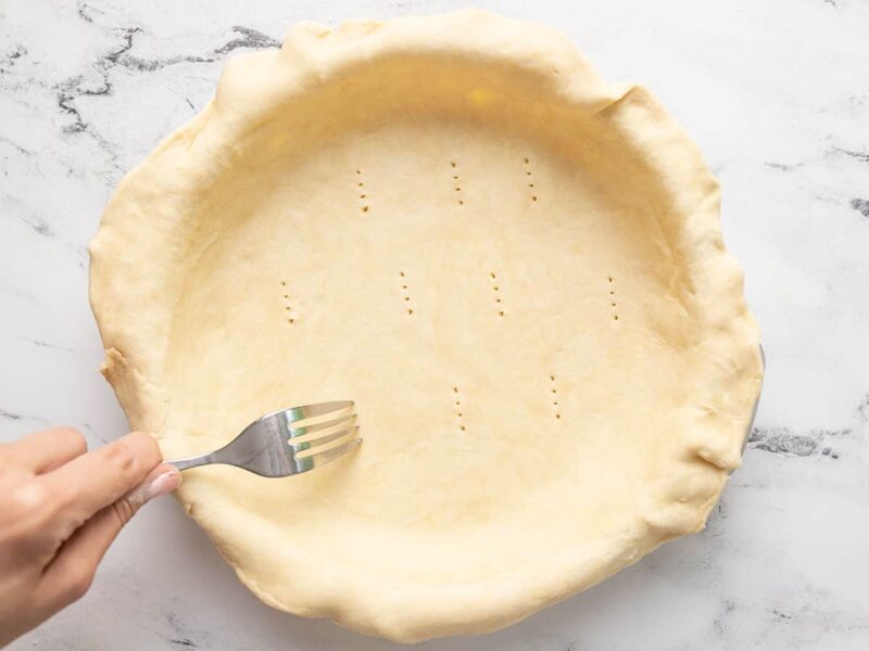 Overhead shot of hand using a fork to dock pie dough.