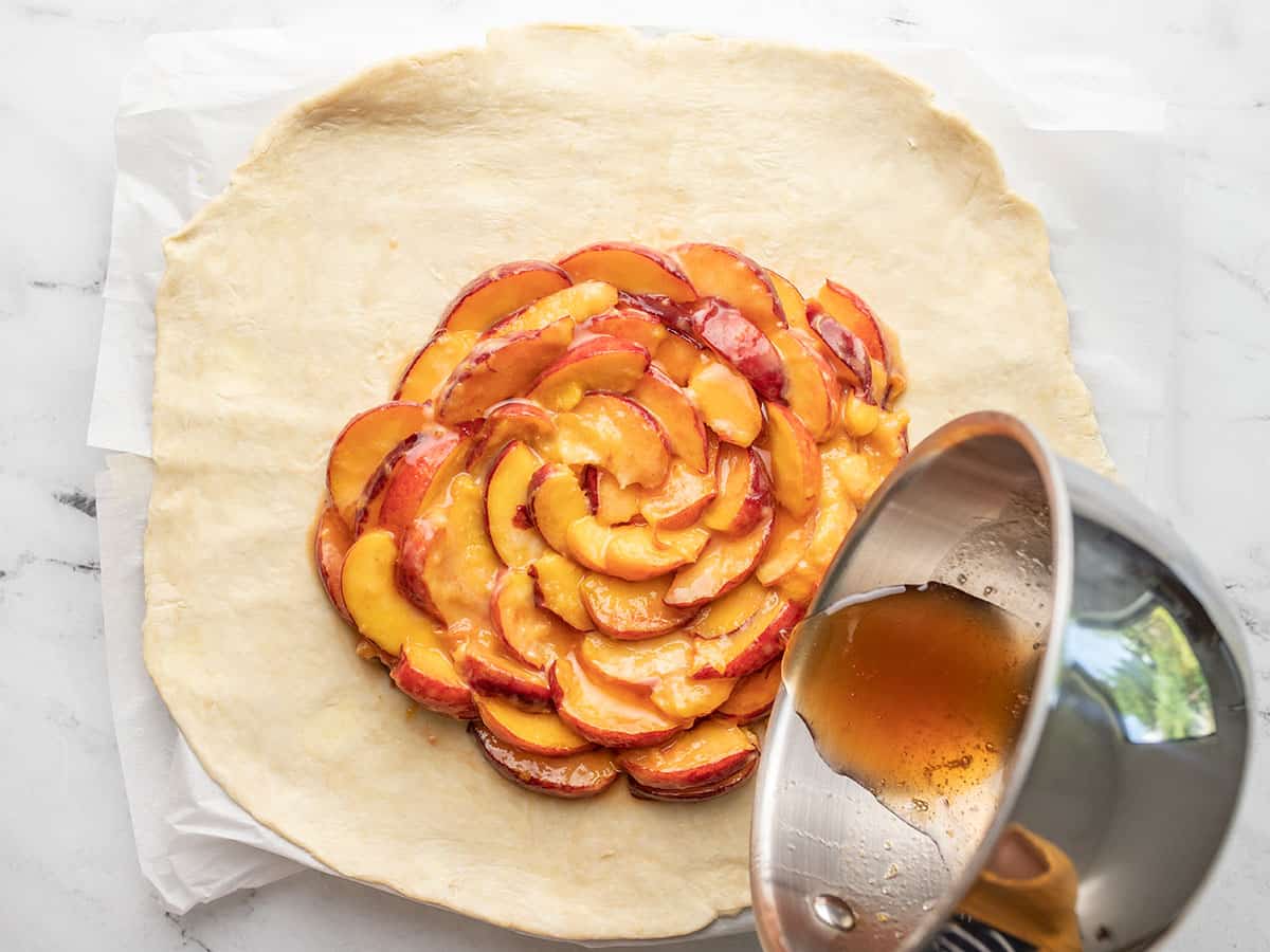 Overhead shot of peach juice caramel being drizzled onto sliced peaches arranged on pie dough.
