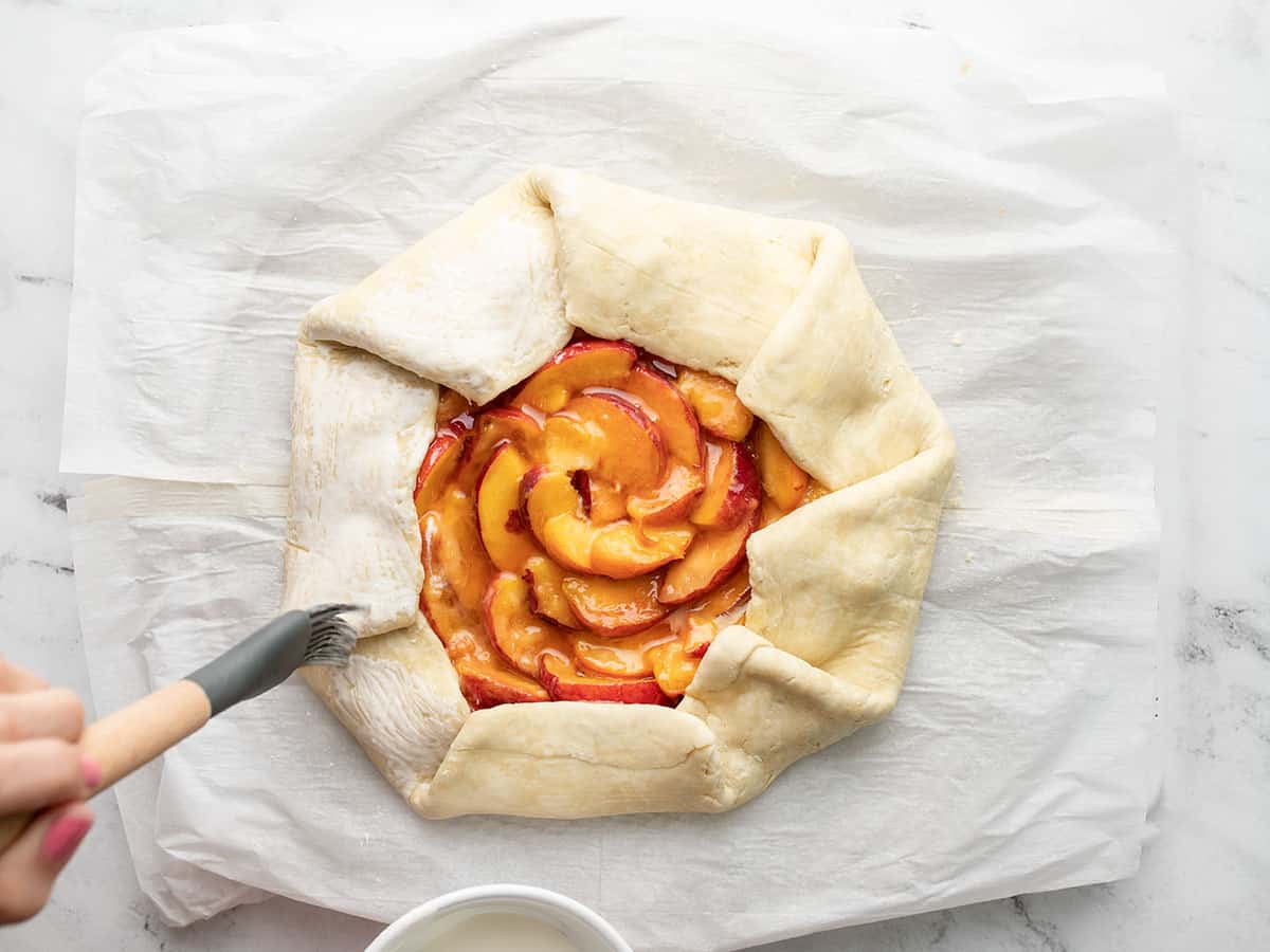 Overhead shot of pie dough edges being folded over peaches.