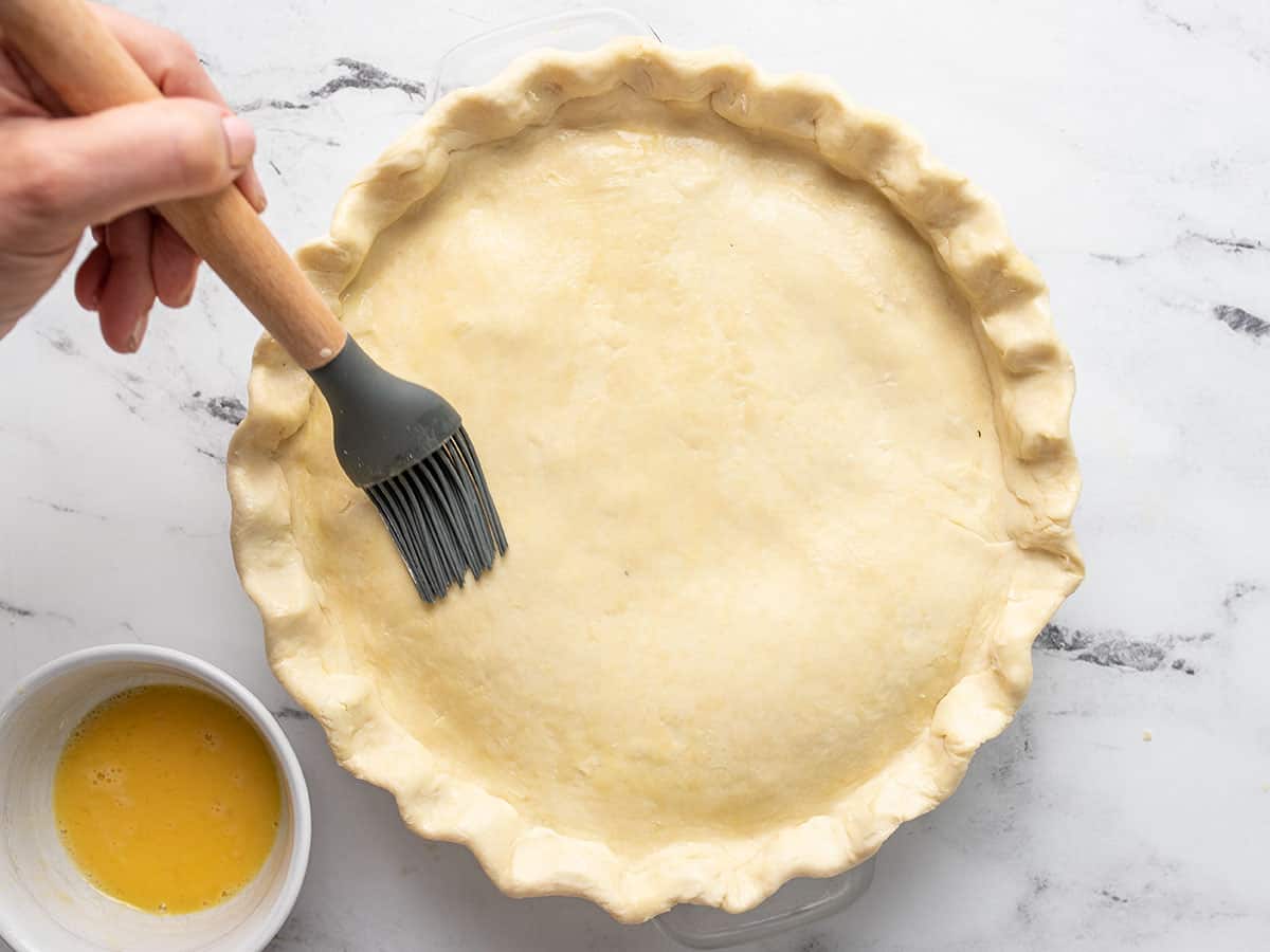 Overhead shot of hand using a pastry brush to place egg wash on pie dough.