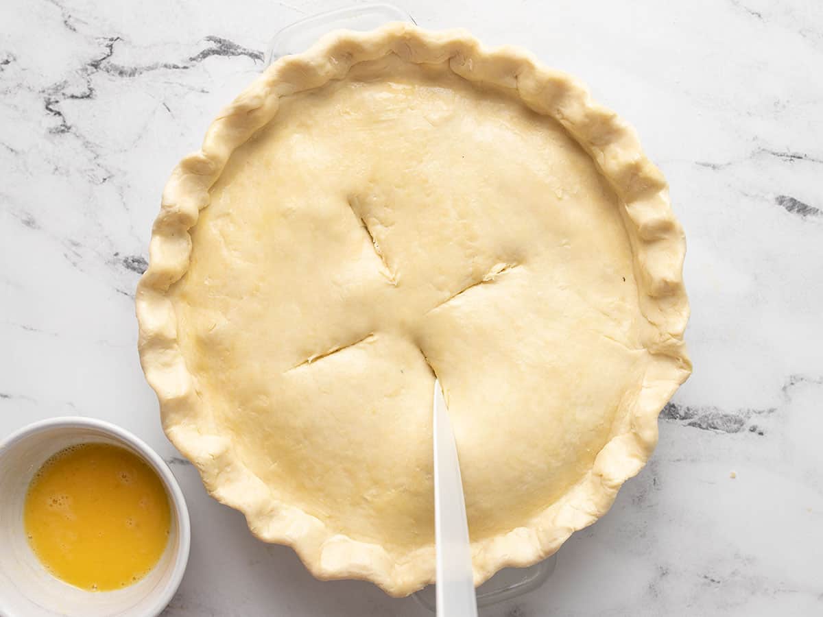 Overhead shot of knifecutting steam vents into uncooked pie top crust.