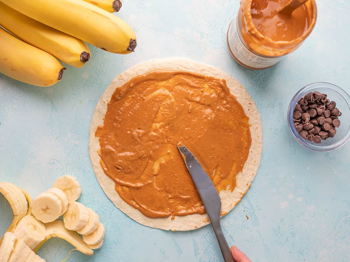 Peanut butter being spread over a tortilla.