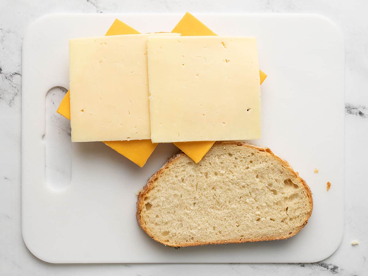 Hava fritözü için peynir dilimleri Bir dilim ekmeğin üzerinde ızgara peynir ve yanında ikinci bir dilim ekmek, bir kesme tahtası üzerinde.