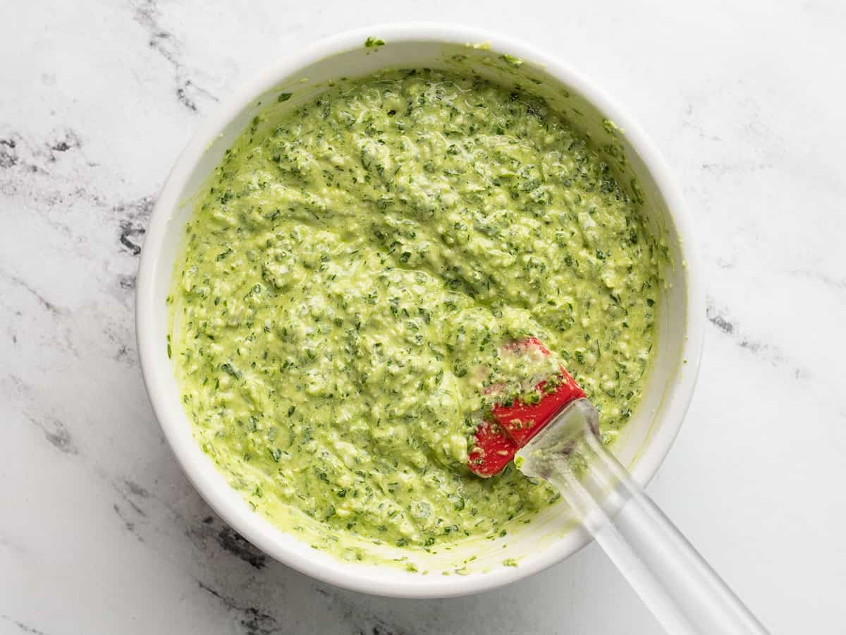 Mayonnaise added to the pesto in a bowl with a spatula.