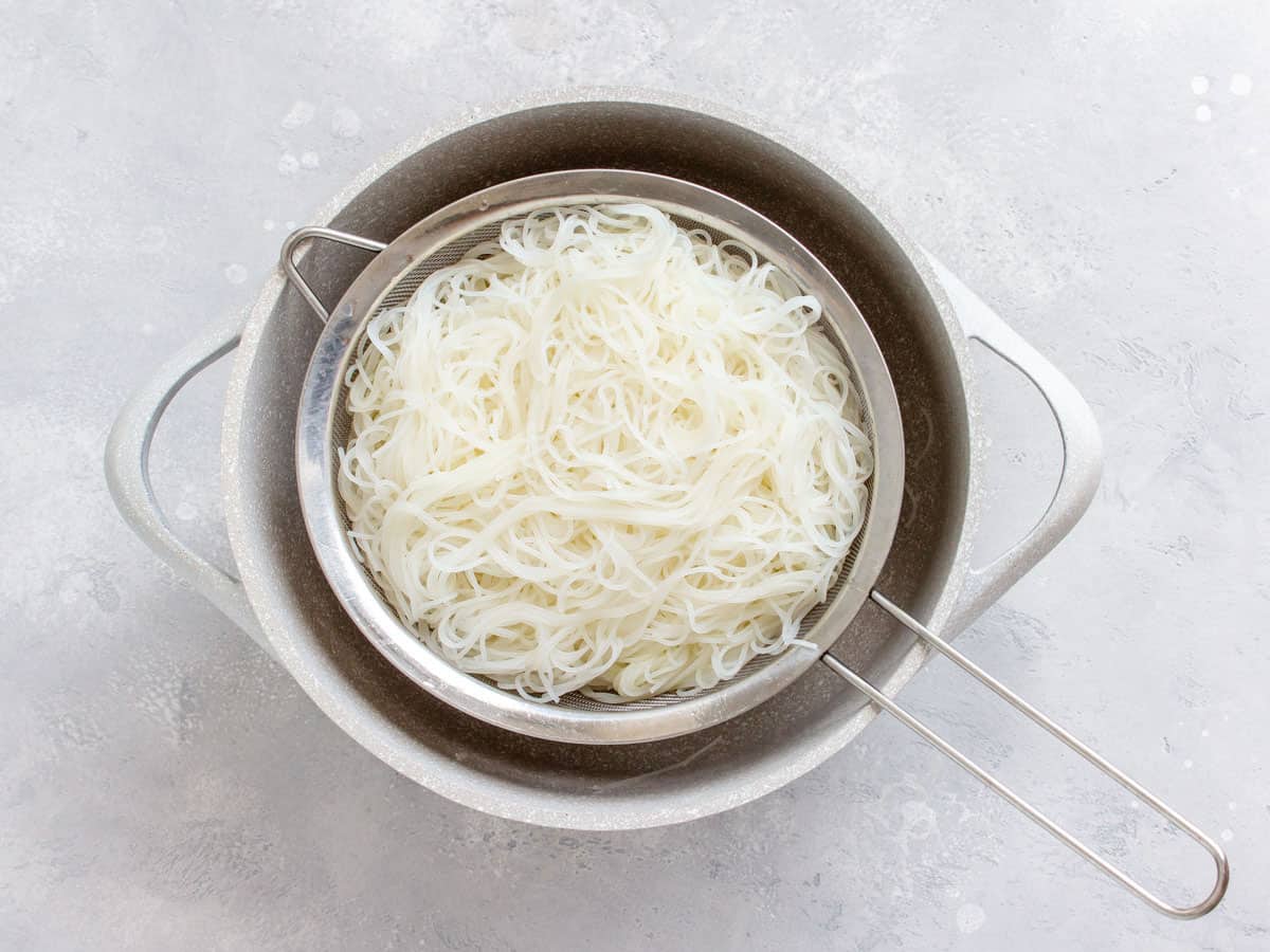 Cooked rice noodles draining in a sieve over a bowl.