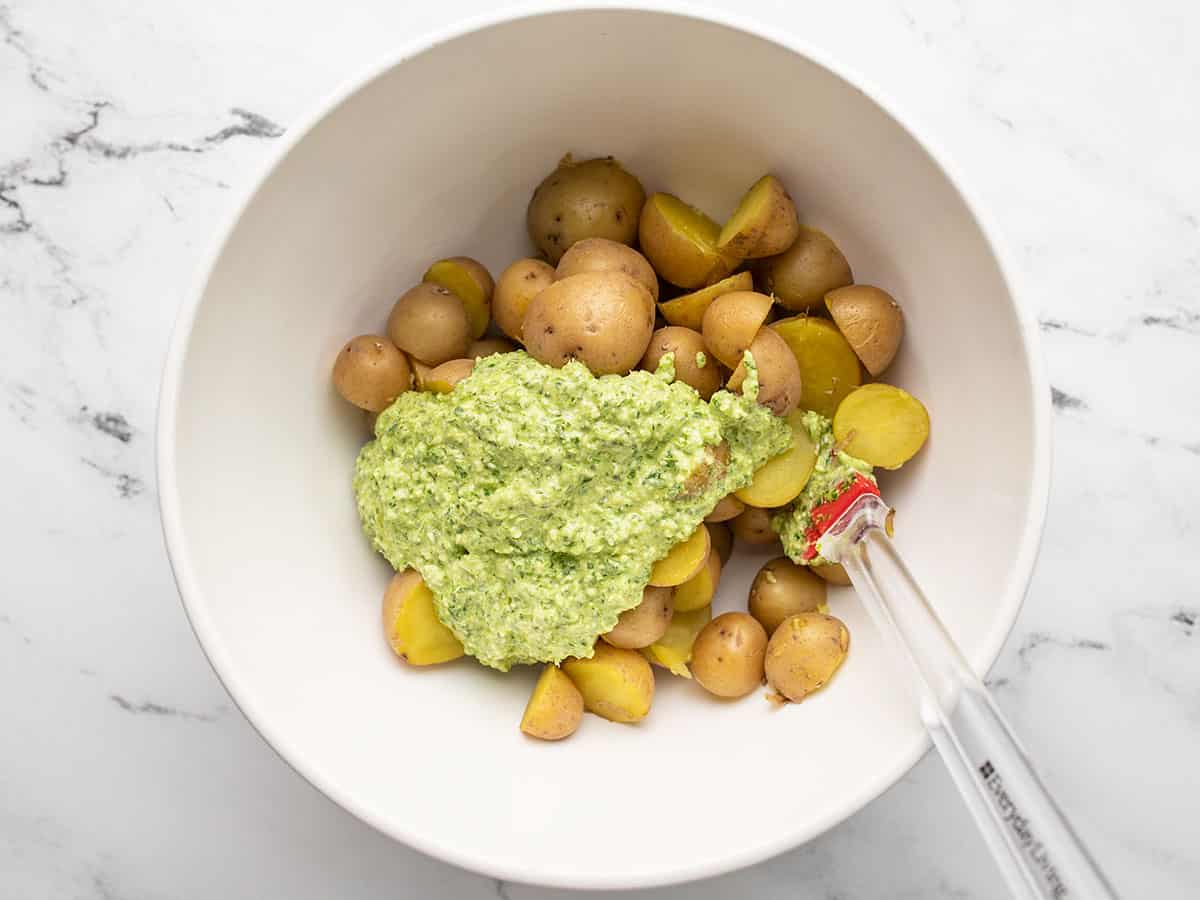 Creamy pesto dressing added to the potatoes in a bowl.