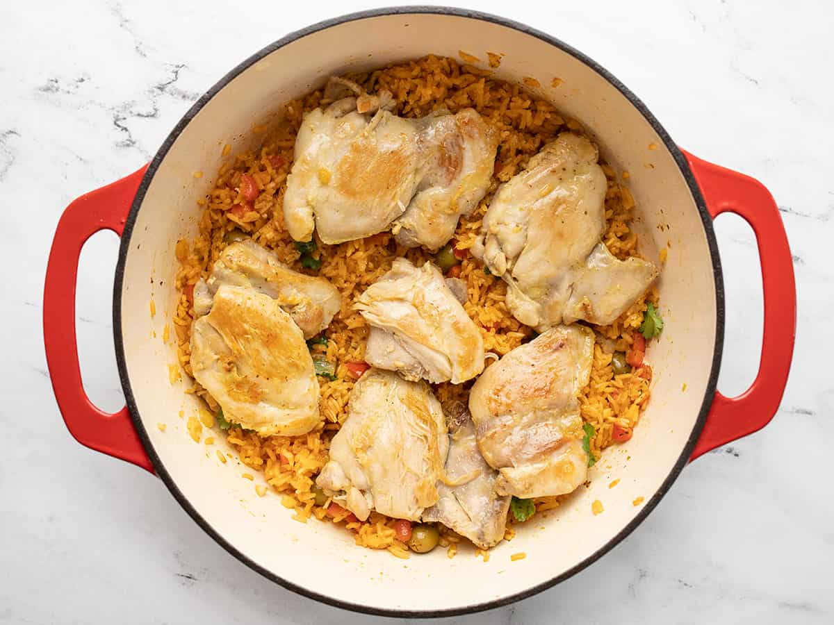 Rice topped with chicken in a red Dutch oven.