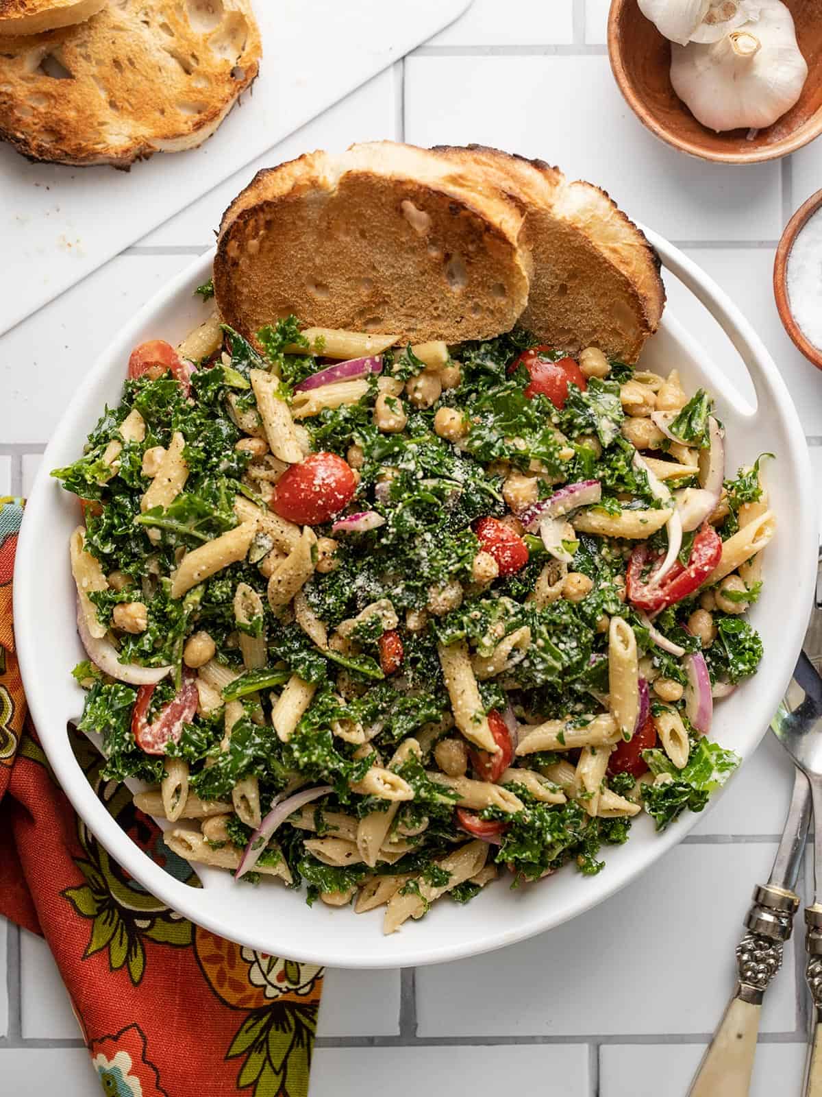 Overhead view of a serving bowl full of kale pasta salad with toast in the side.